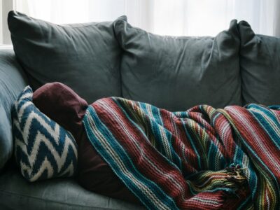 person lying on sofa under covers feeling sick